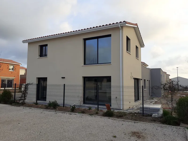 Maison à étage aux façades claires. Vue extérieure d’une maison avec de larges ouvertures et une toiture en tuiles.