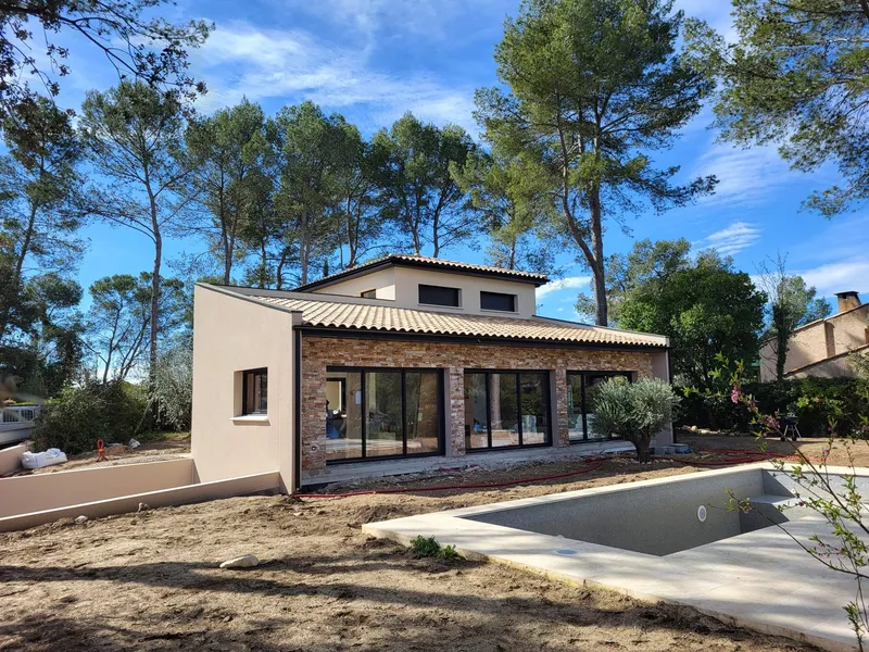 Maison avec terrasse couverte. Façades claires, baies vitrées et terrasse abritée ouverte sur le jardin.