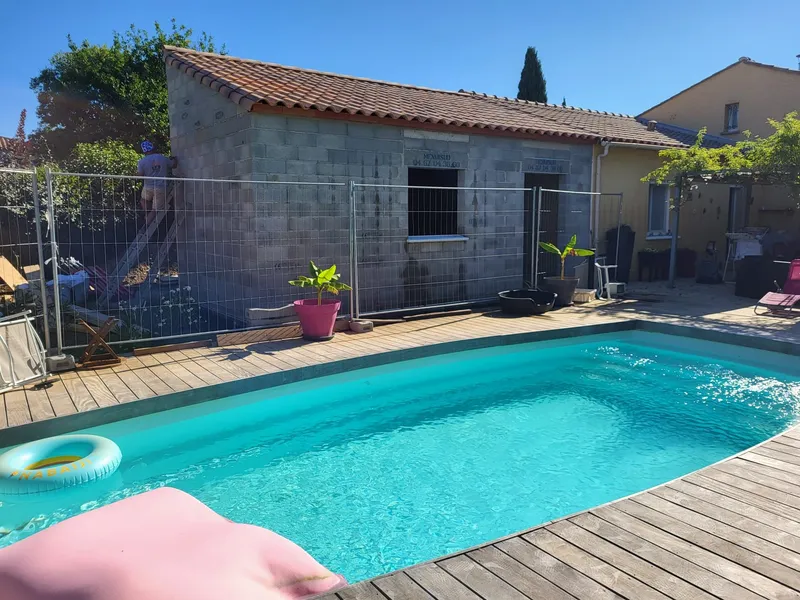 Piscine et bâtiment annexe. Bassin extérieur bordé d’une terrasse, devant une annexe maçonnée.